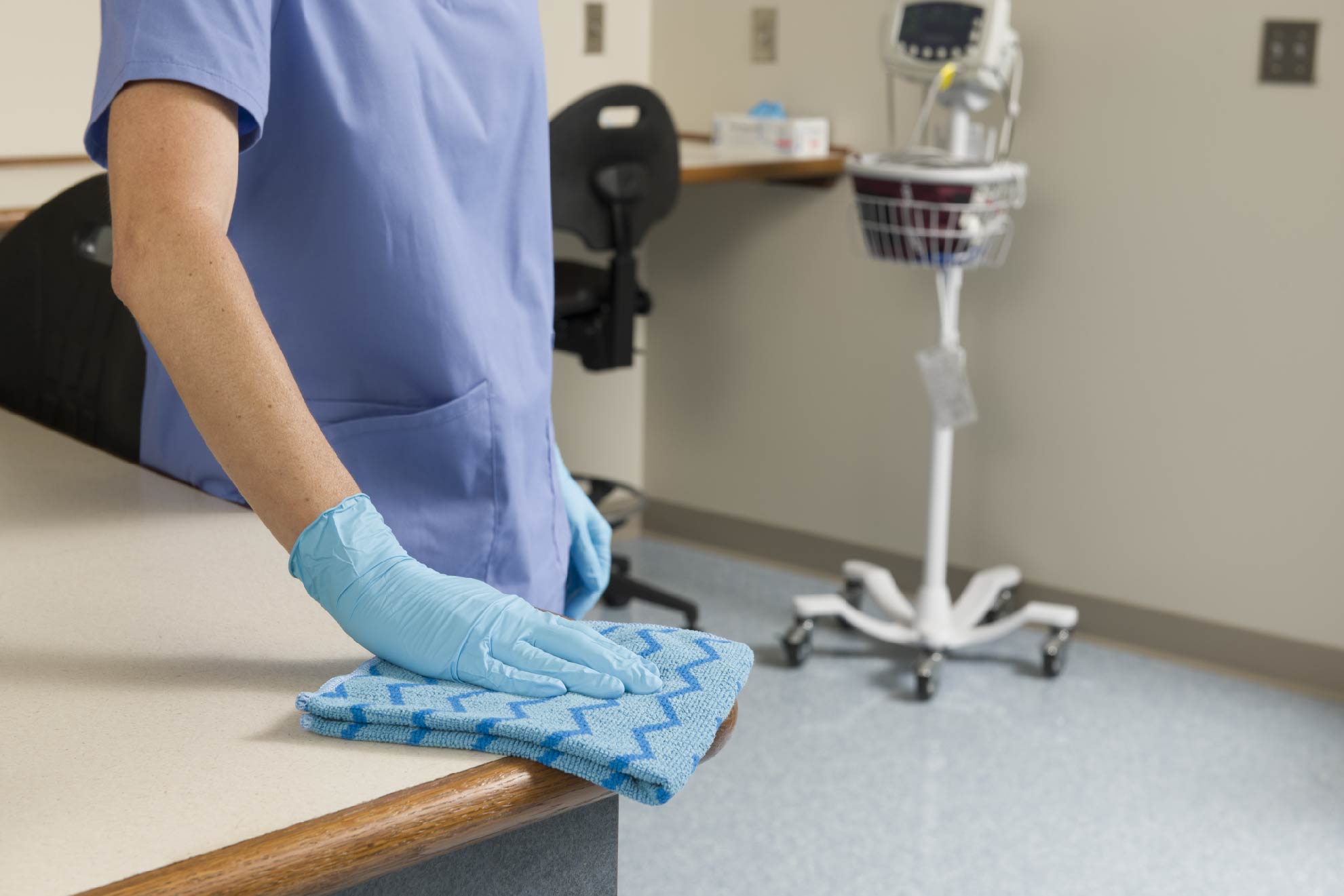 Healthcare worker cleaning a surface with a blue microfiber cloth in a hospital or clinic.