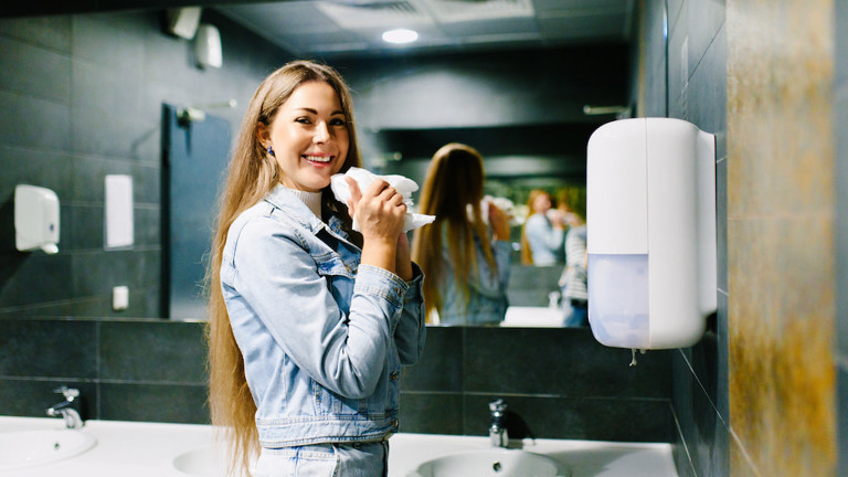 A woman using a wall-mounted paper towel dispenser in a public restroom