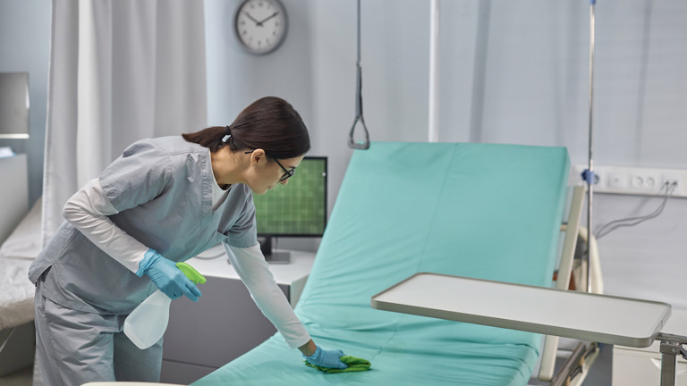 A healthcare professional sanitizing a hospital bed.