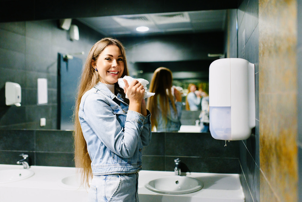 A woman using a wall-mounted paper towel dispenser in a public restroom
