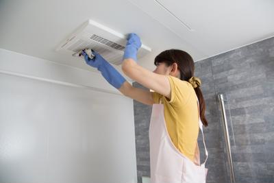 A woman wearing gloves and an apron is deep cleaning a ceiling fan